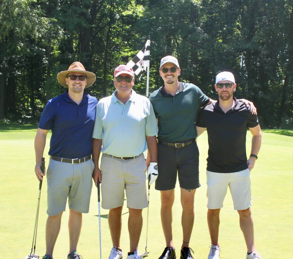 4 alumni take a team picture infront of the hole